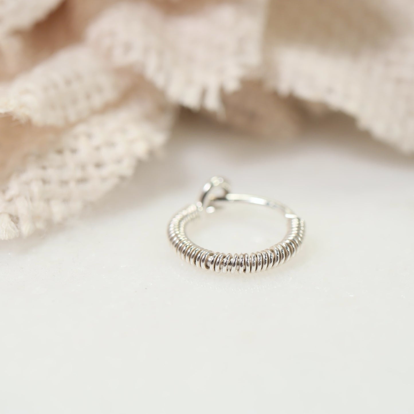 A single tiny hoop earring made of silver, displayed against a textured background.