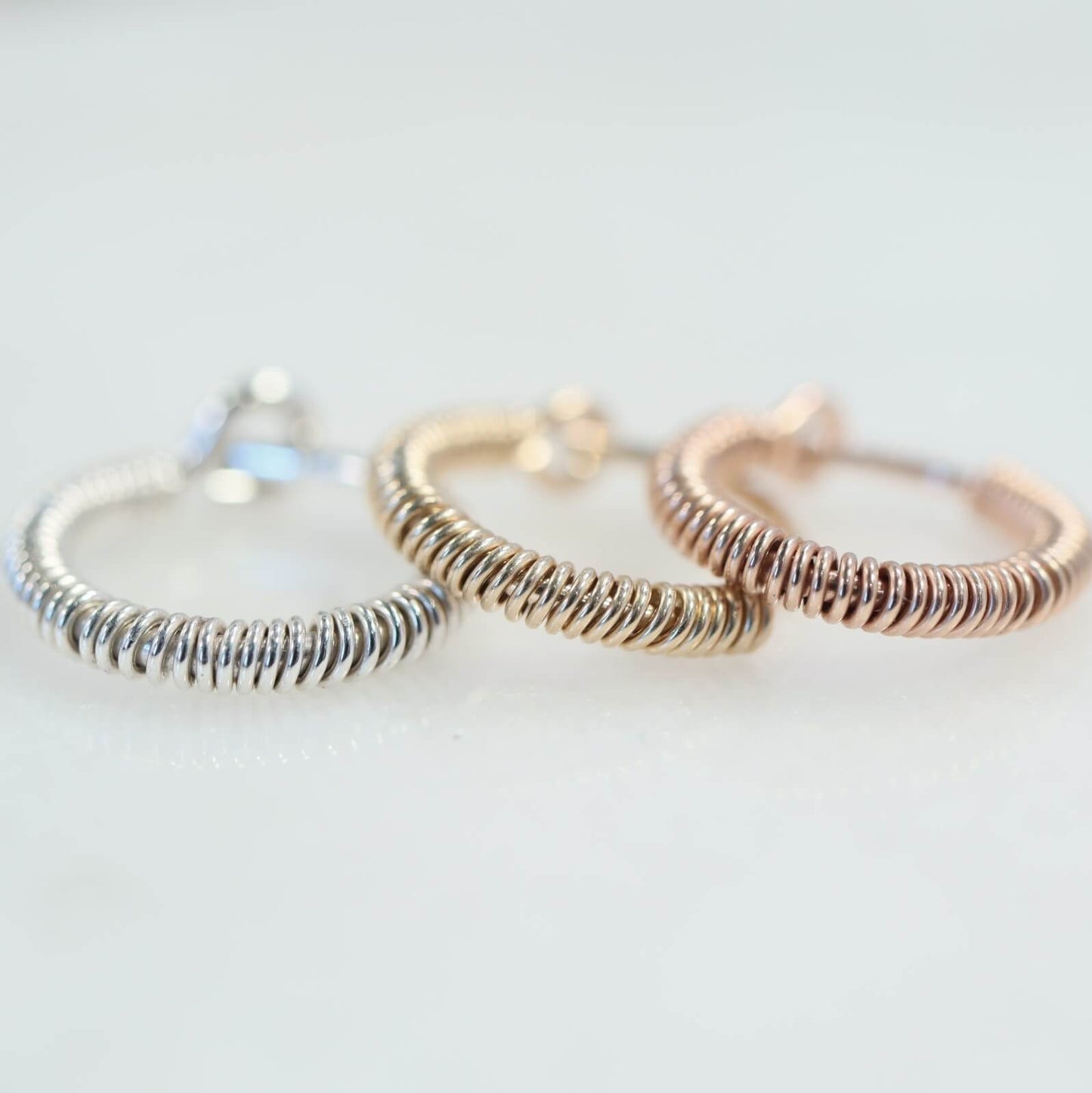 three wrapped design hoops silver gold and pink gold on a white background