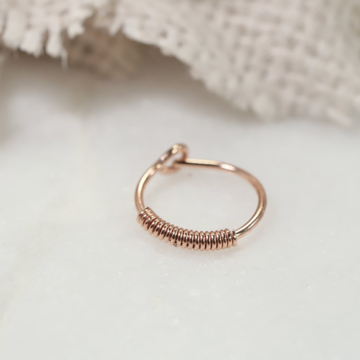 A single hoop earring with a wrapped texture, displayed on a white background, potentially adjustable with a click closure.