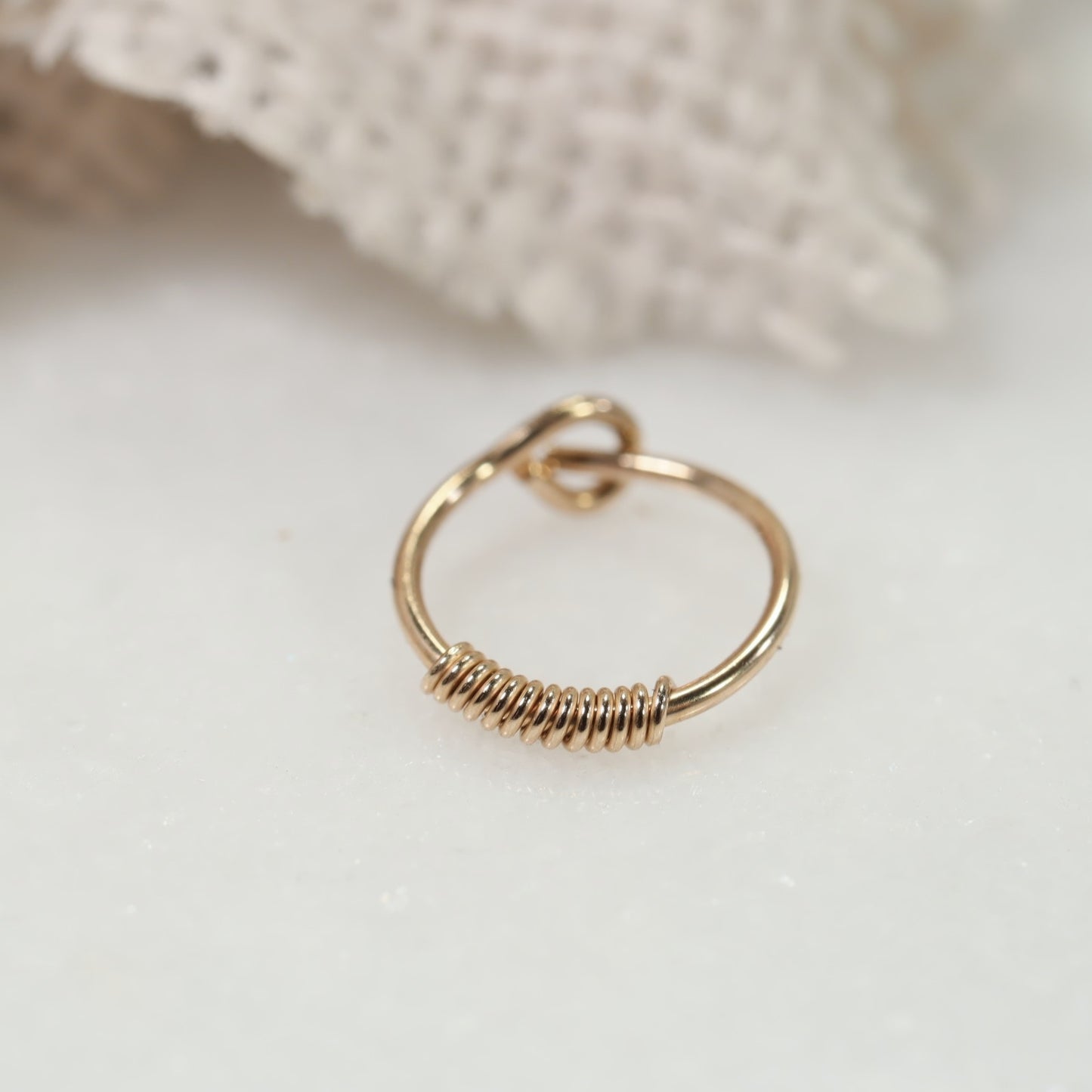 A gold hoop earring with a wrapped texture, displayed on a white background, potentially adjustable with a click closure.