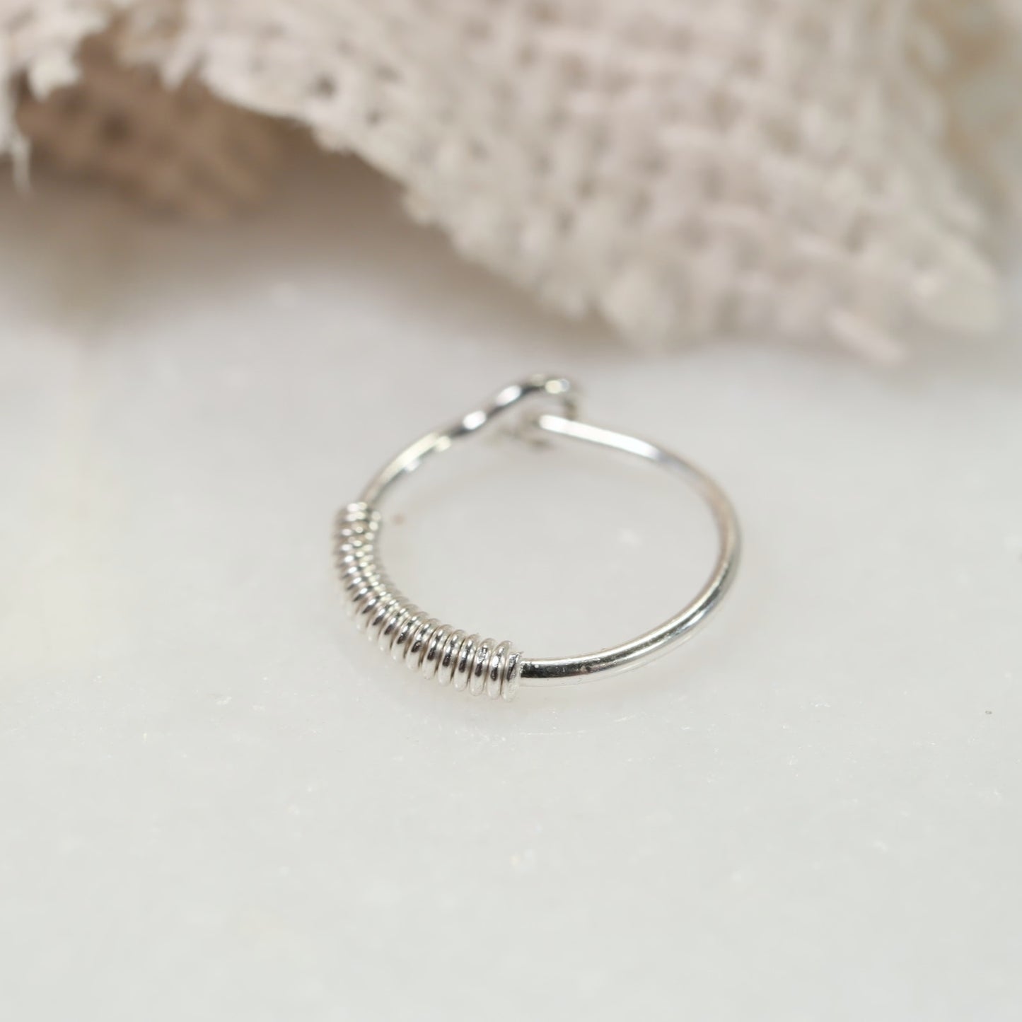 A silver hoop earring with a wrapped texture, displayed on a white background, potentially adjustable with a click closure.