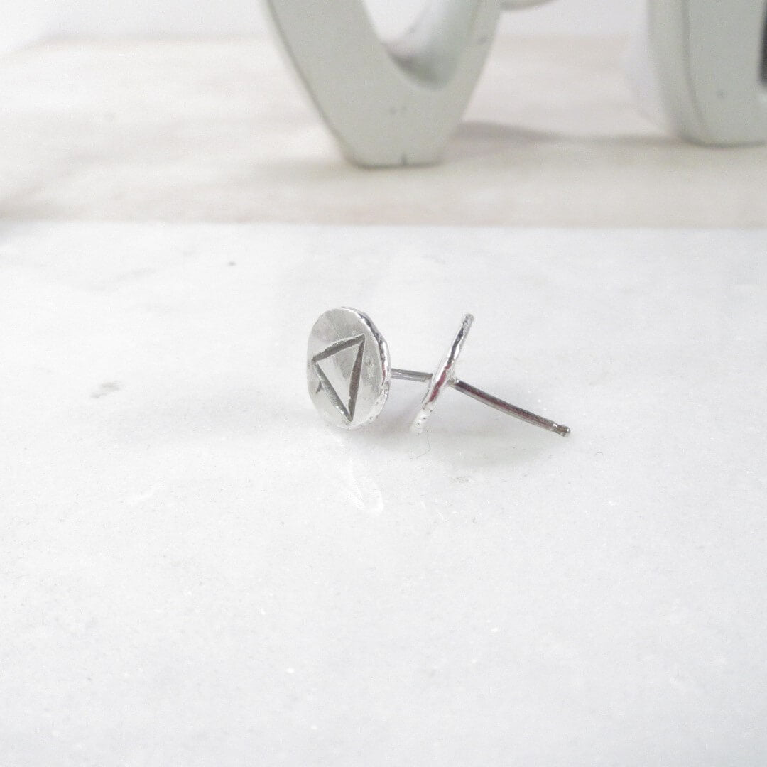 Close-up of solid silver stud earrings with a air design, placed on a white surface.