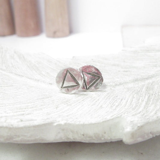 Close-up of solid silver stud earrings with a geometric design, placed on a white surface.