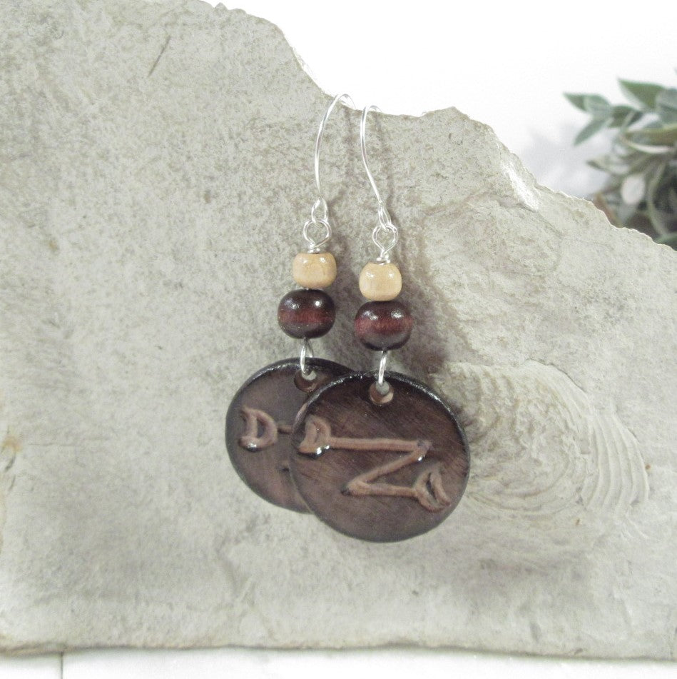 Pair of earrings with circular brown charms and beads on a stone surface