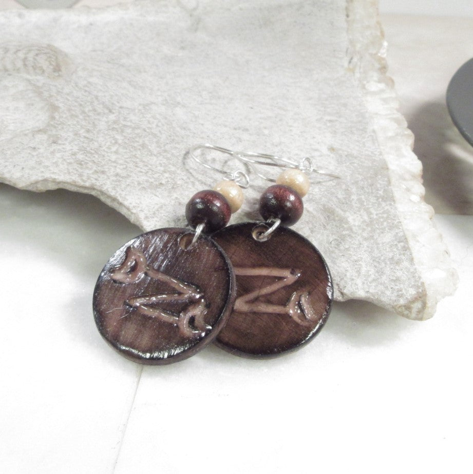 Pair of brown circular earrings with engraved designs on a white surface.