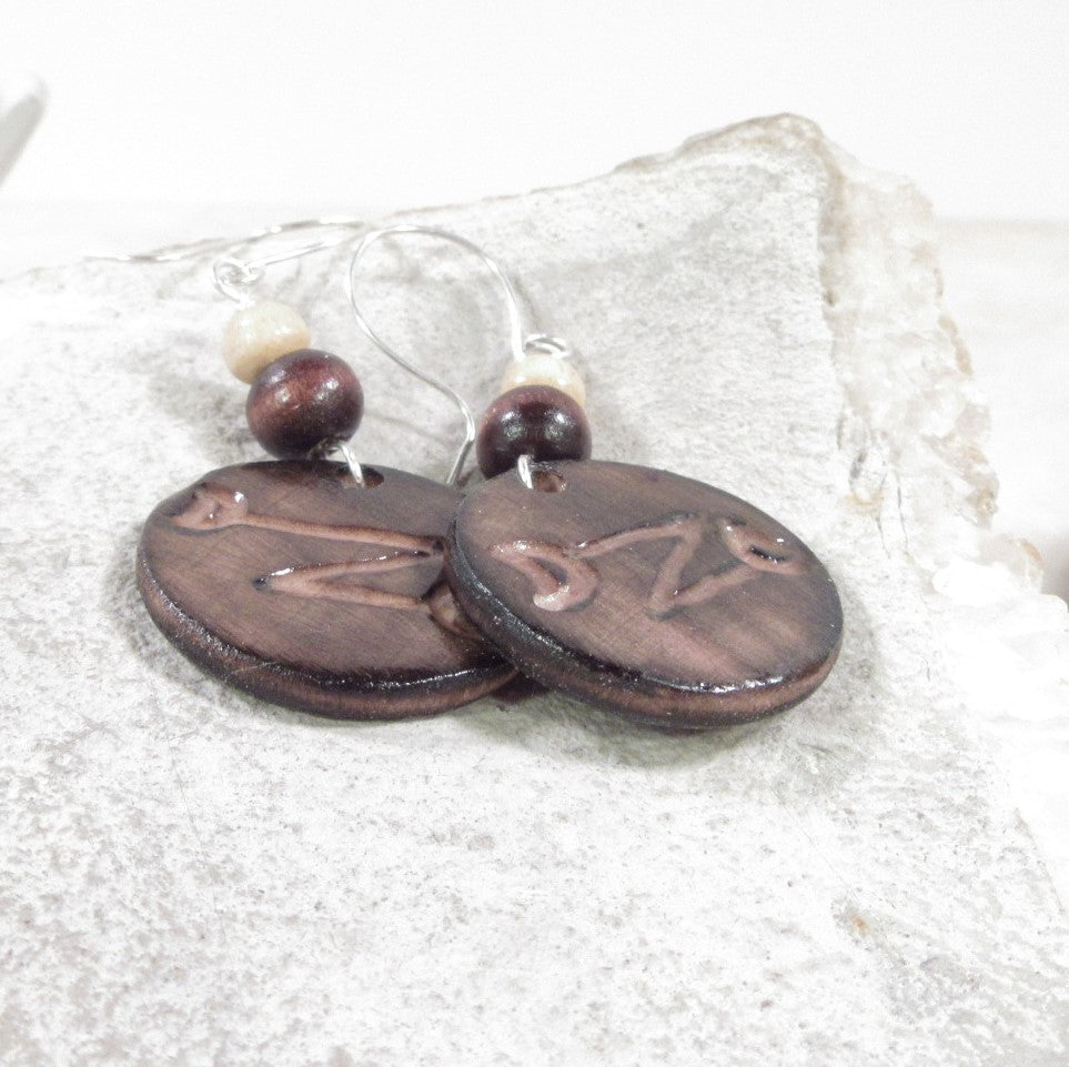 Pair of brown ceramic earrings with engraved initials on a textured white surface