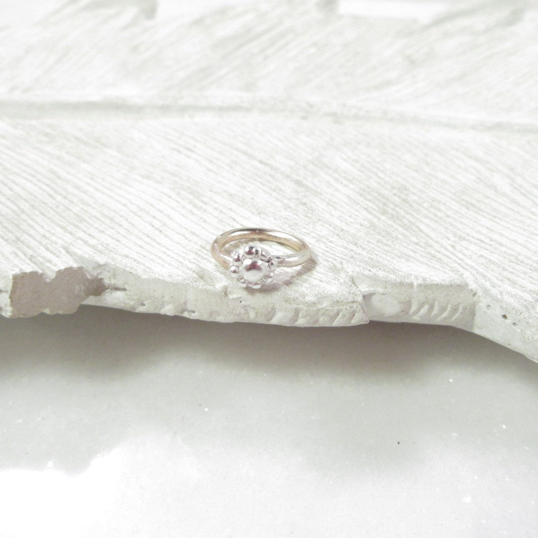 Silver tragus hoop with a flower on a textured white surface