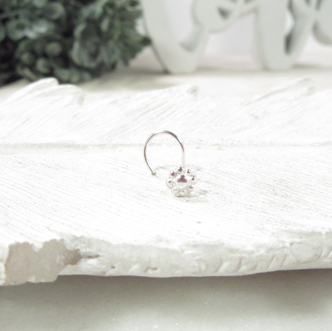 Silver nose stud on a textured white surface with a blurred background
Details