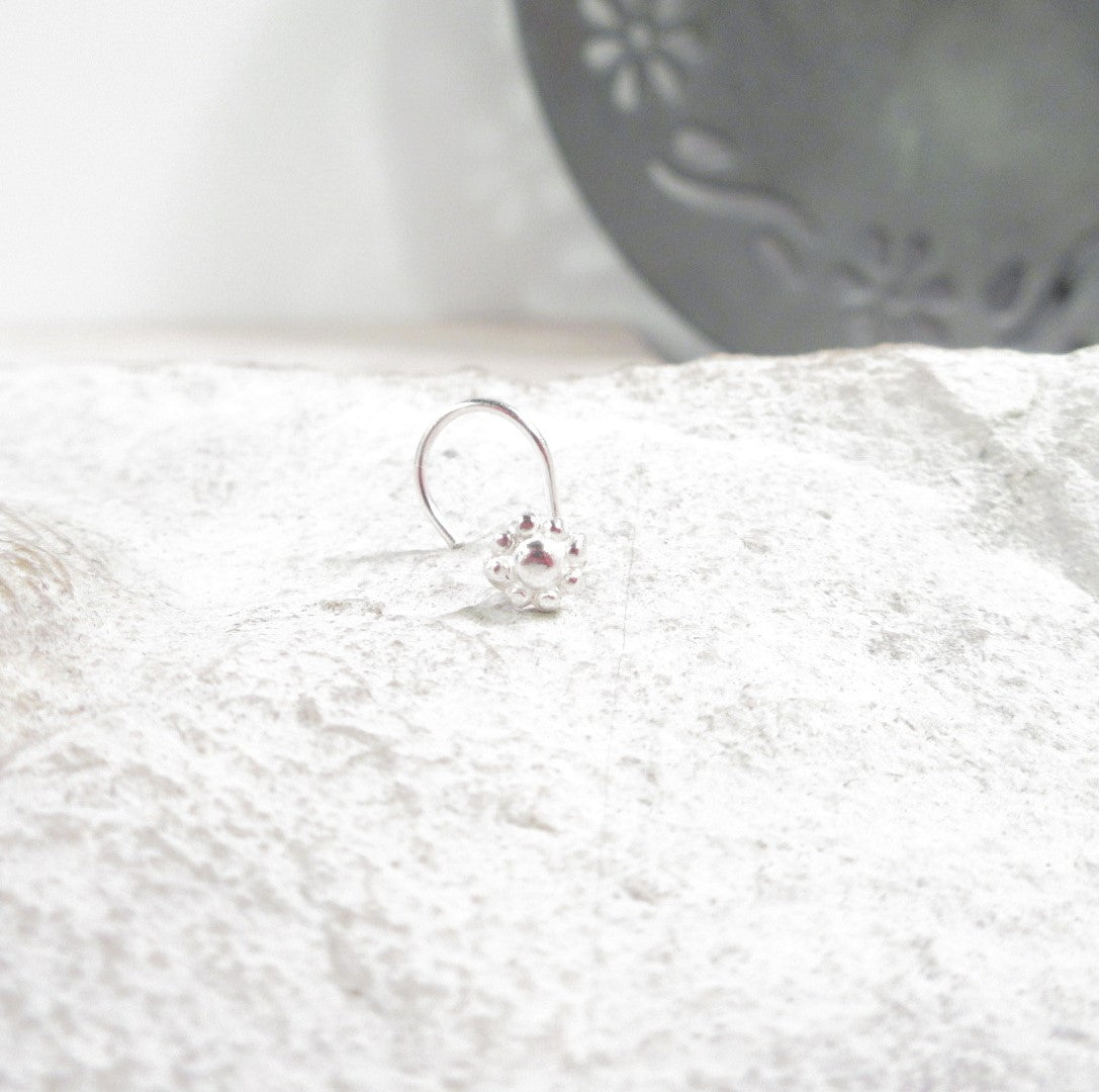 Silver nose stud with a flower on a textured white surface
