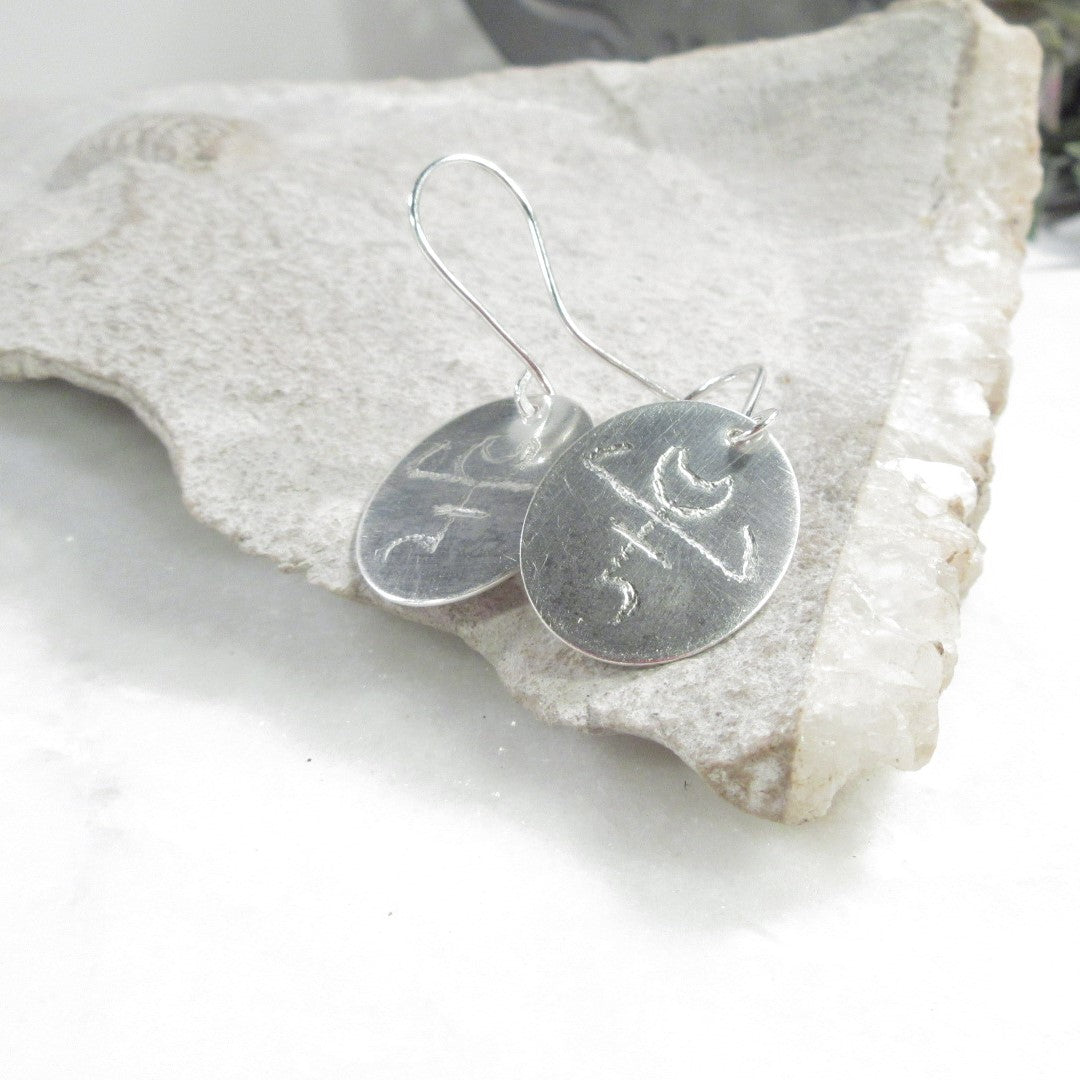 Silver earrings with engraved designs on a stone surface