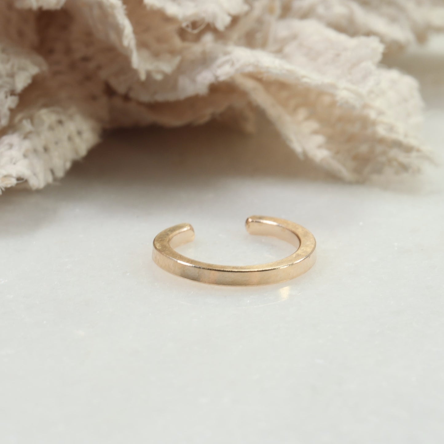 Gold ring on a white surface with a textured beige fabric background