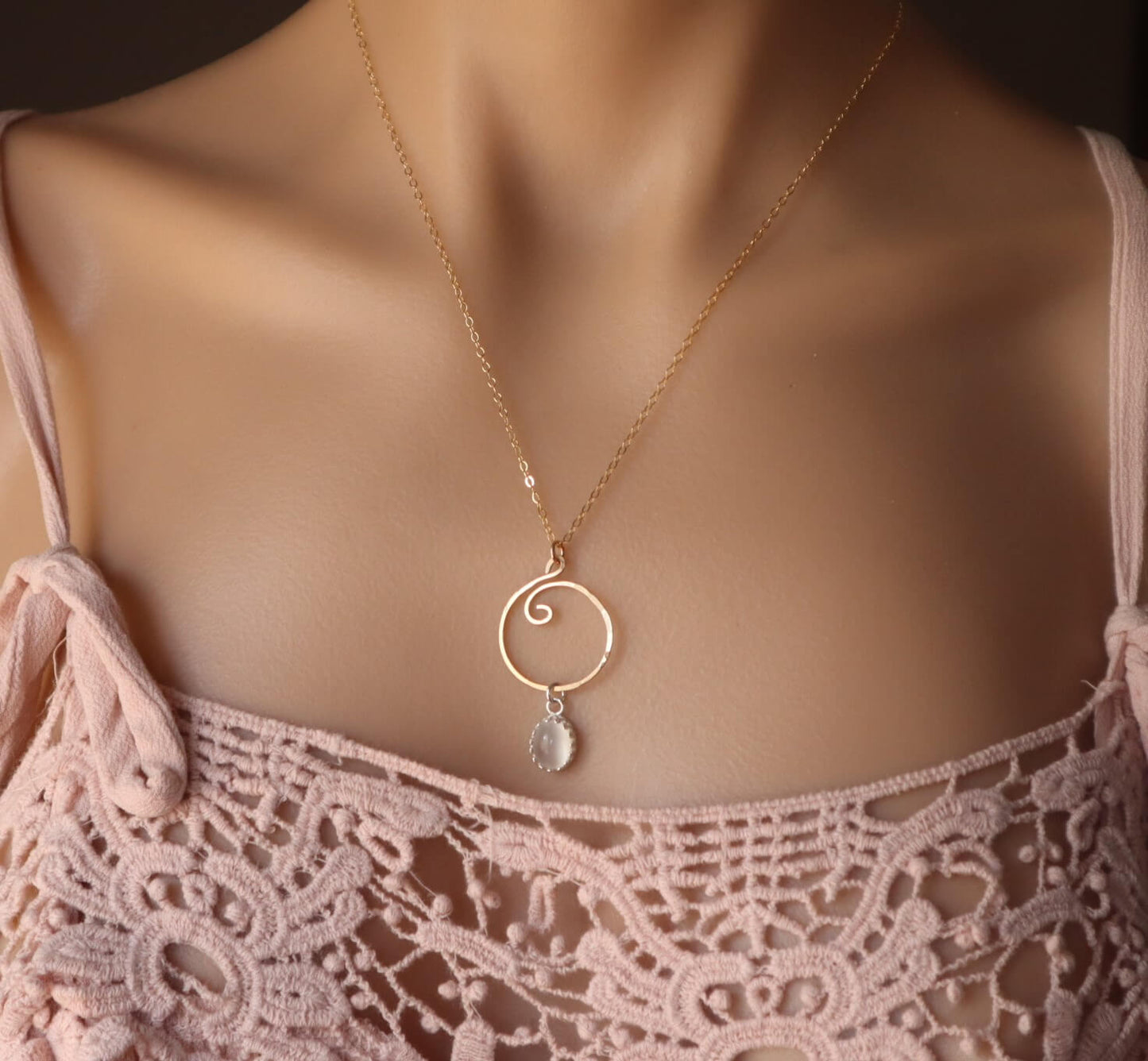 Gold necklace with a circular pendant on a model wearing a pink lace top.