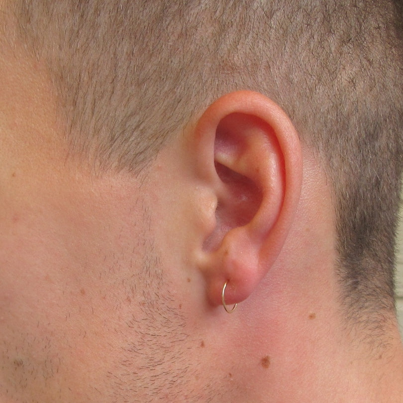 A close-up image of a man's ear wearing a single hoop earring with a hammered texture.