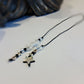 A delicate black cord Bookmark featuring a central white translucent bead, small black and clear spacer beads, and two dangling star charms, one silver-toned and one iridescent white, displayed on a light surface.