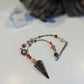 A beaded crystal pendulum featuring a large garnet crystal pendant, small red beads, and silver-toned metal charms, displayed on a white surface.