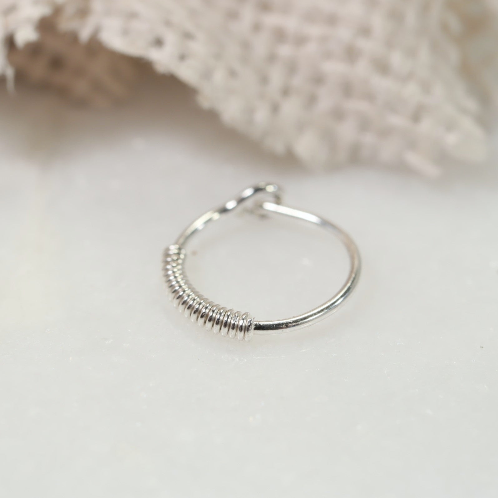 A silver hoop earring with a wrapped texture, displayed on a white background, potentially adjustable with a click closure.