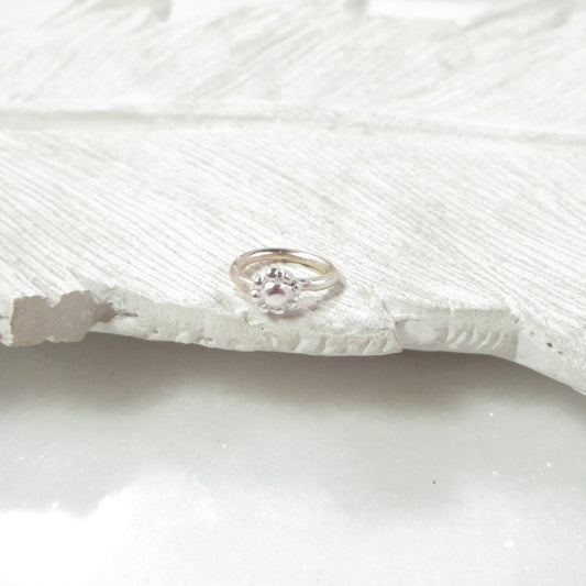 Silver tragus hoop with a flower on a textured white surface