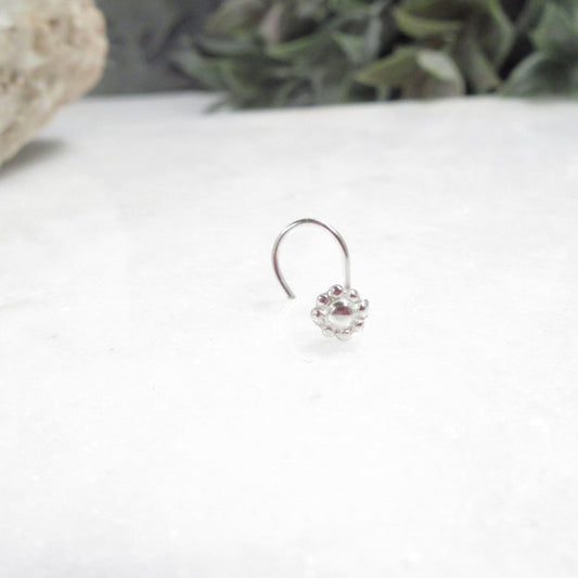 Silver flower nose ring on a white surface with greenery in the background