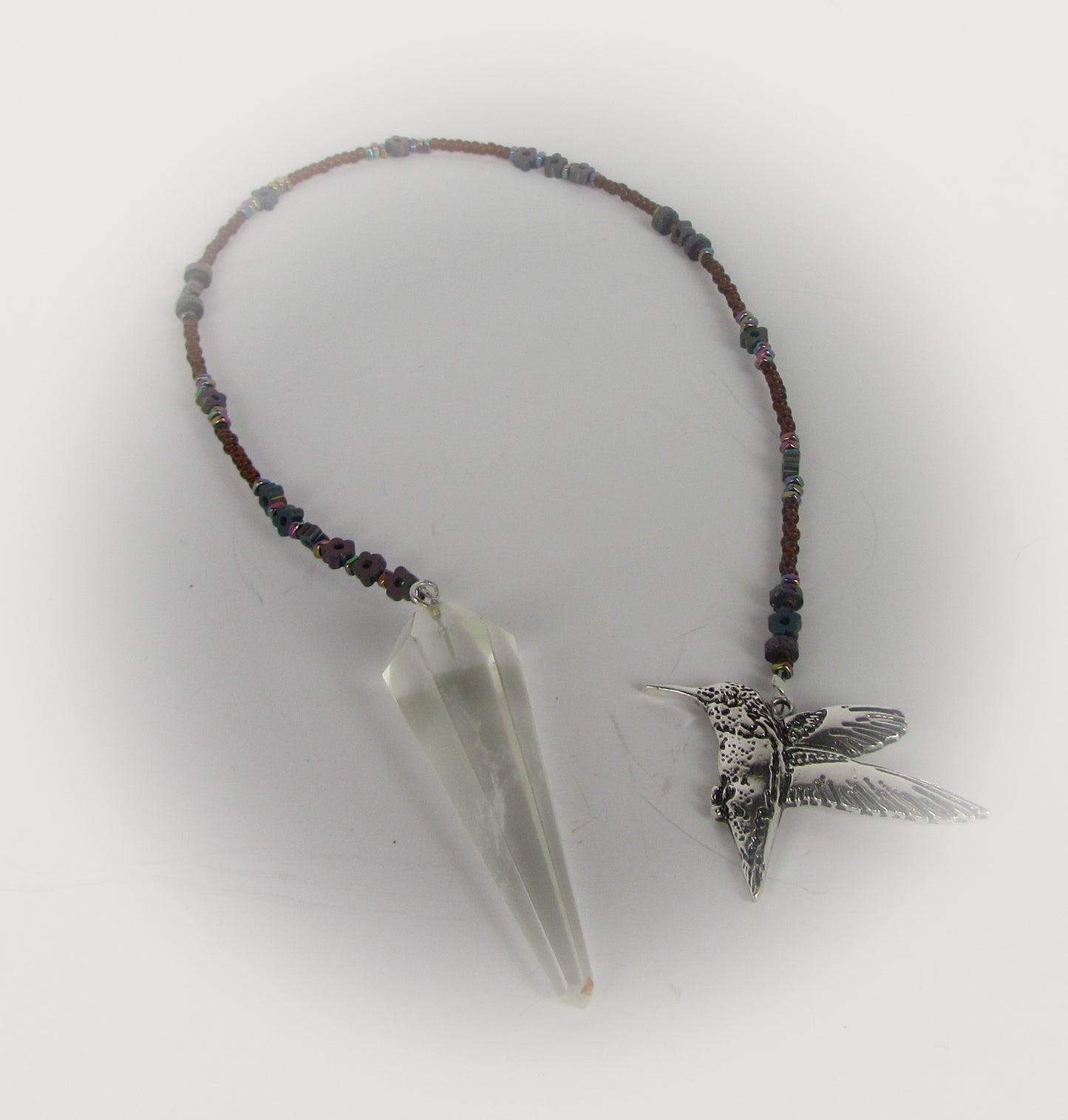 Pendulum with beaded chain, crystal pendant, and silver hummingbird charm on a white background