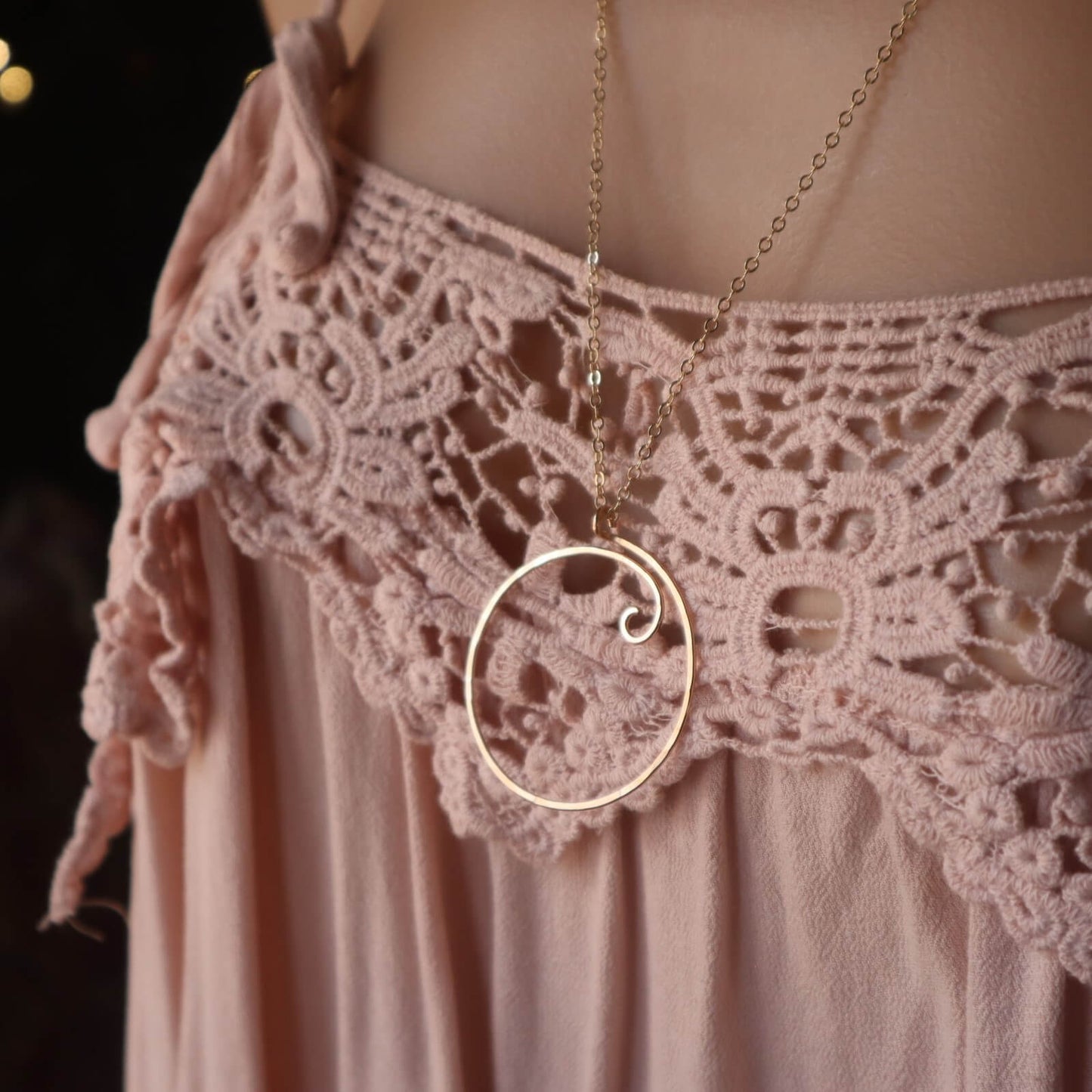 Charm holder necklace on a pink lace garment against a dark background