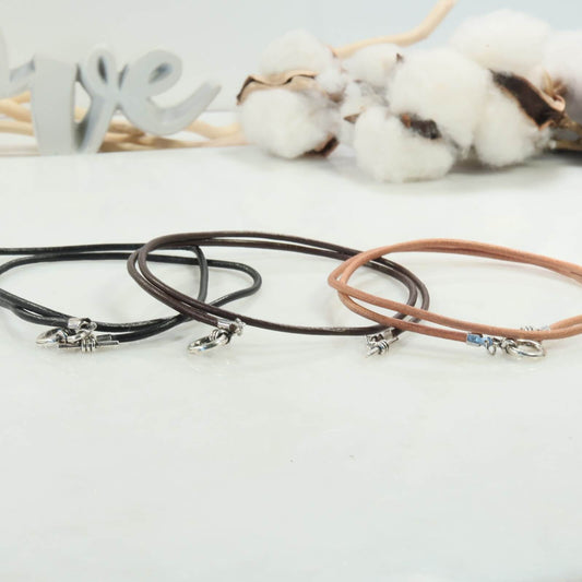 Three leather necklaces on a white surface with cotton and 'LOVE' letters in the background.
