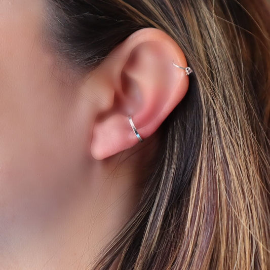 Close-up of an ear with two silver hoop earrings against a blurred background